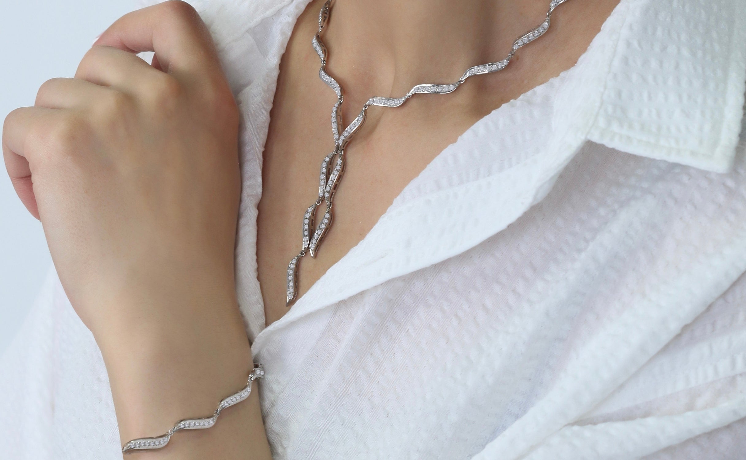 Silver bracelet and necklace on a person's wrist and chest against a white background